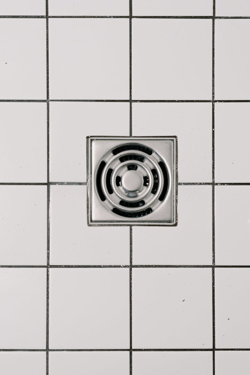 Top view of white ceramic tile floor with stainless steel square shaped cover of drain in contemporary shower
